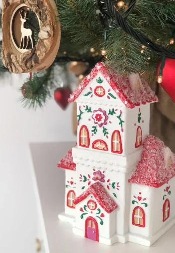 Casita navideña de porcelana blanca y roja junto a un árbol de Navidad con luces