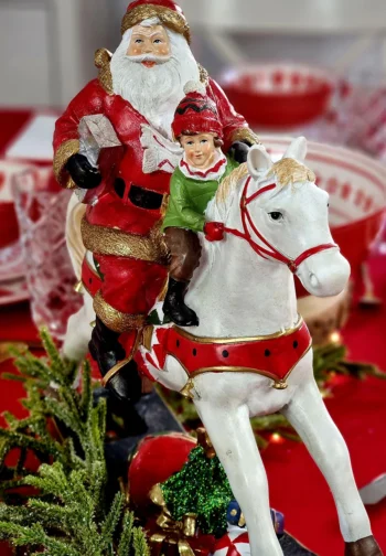 Figura de Papá Noel con un niño sobre un caballo balancín, en una mesa navideña